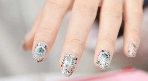 Hand wearing whimsical cat nail art wraps with illustrated kittens and floral design