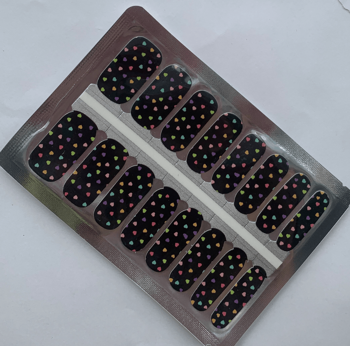 Non-UV nail wraps sheet with black background and rainbow heart pattern for at-home manicure