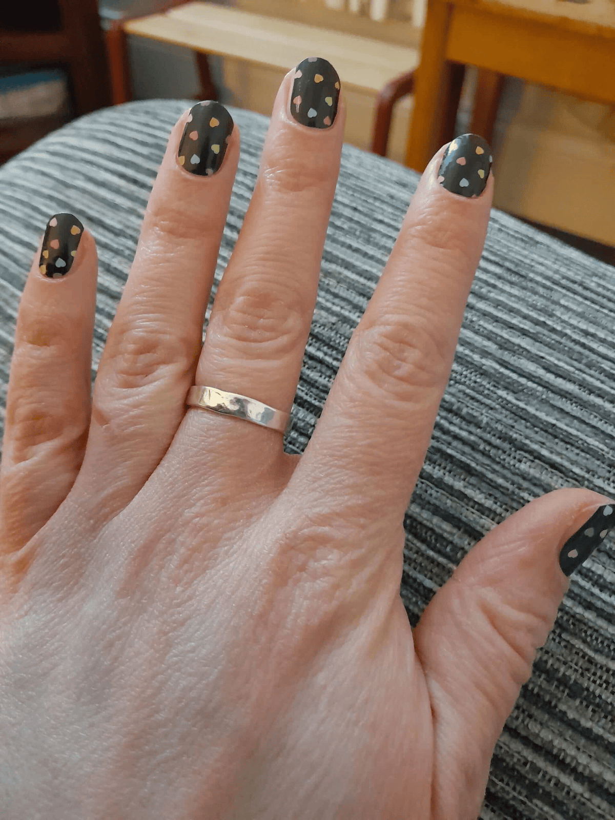 Black matte nail wraps with scattered tiny pastel heart print, on short round nails