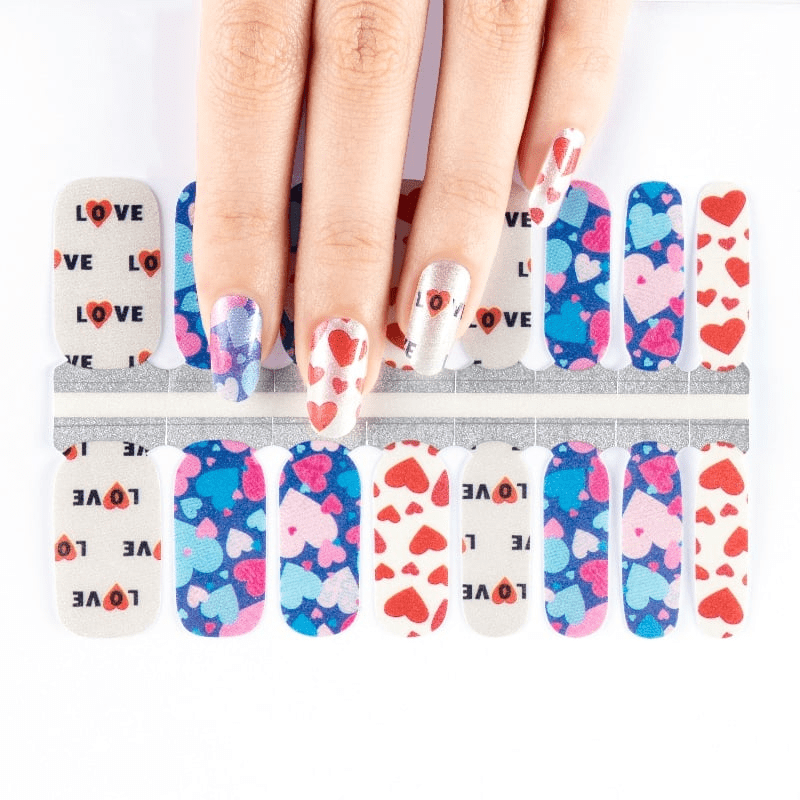 Hands applying heart pattern nail wraps with blue and pink romantic Valentine's designs