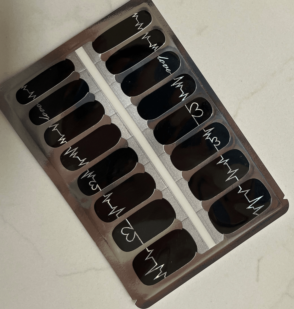 Black non-UV nail wraps with white heart typography arranged in packaging sheet
