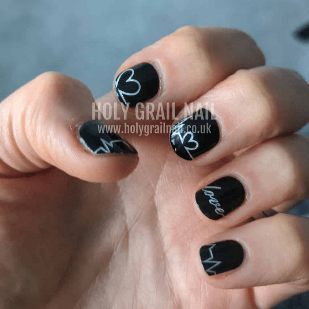 Black manicure wraps with white heart designs worn on hand showing nail art