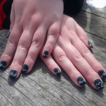Black nail wraps with white heart typography on hands gothic manicure design
