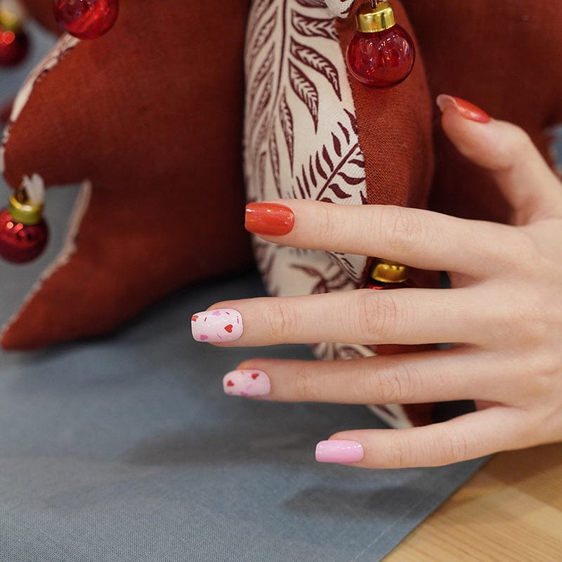 Pink heart nail wraps on hand with red accent nails for romantic at-home manicure