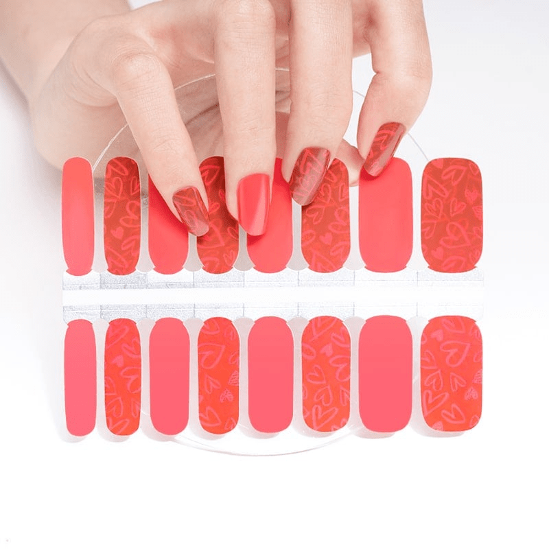 Hand selecting from coral red gradient nail wraps sheet with heart patterns