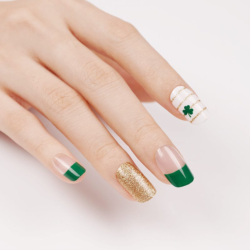 Close-up hand showing green and gold Irish-themed nail wraps with clover accent designs