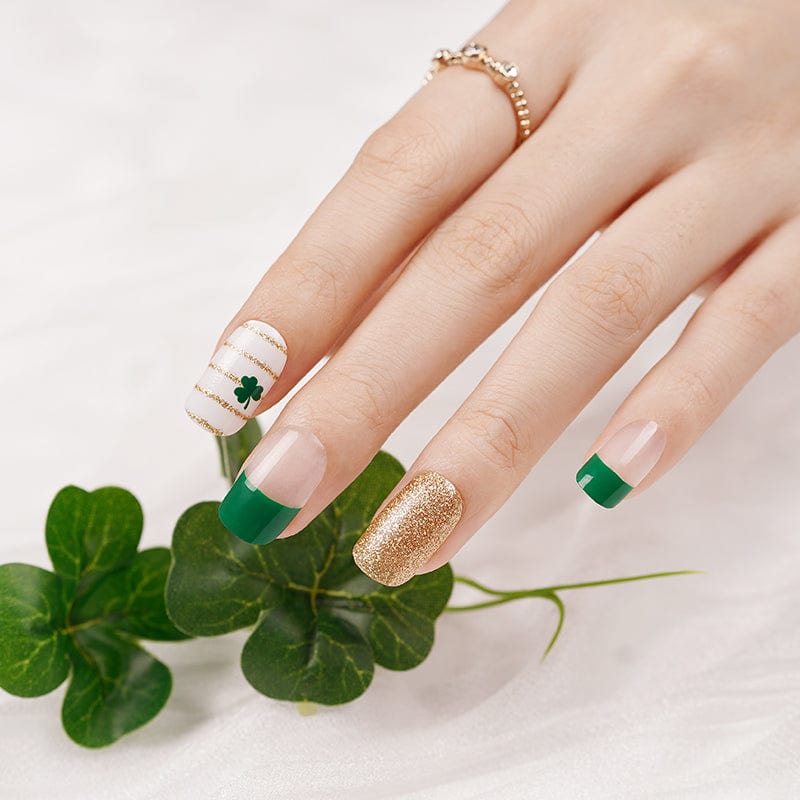 Hand with green French tip nail wraps featuring gold glitter and shamrock designs