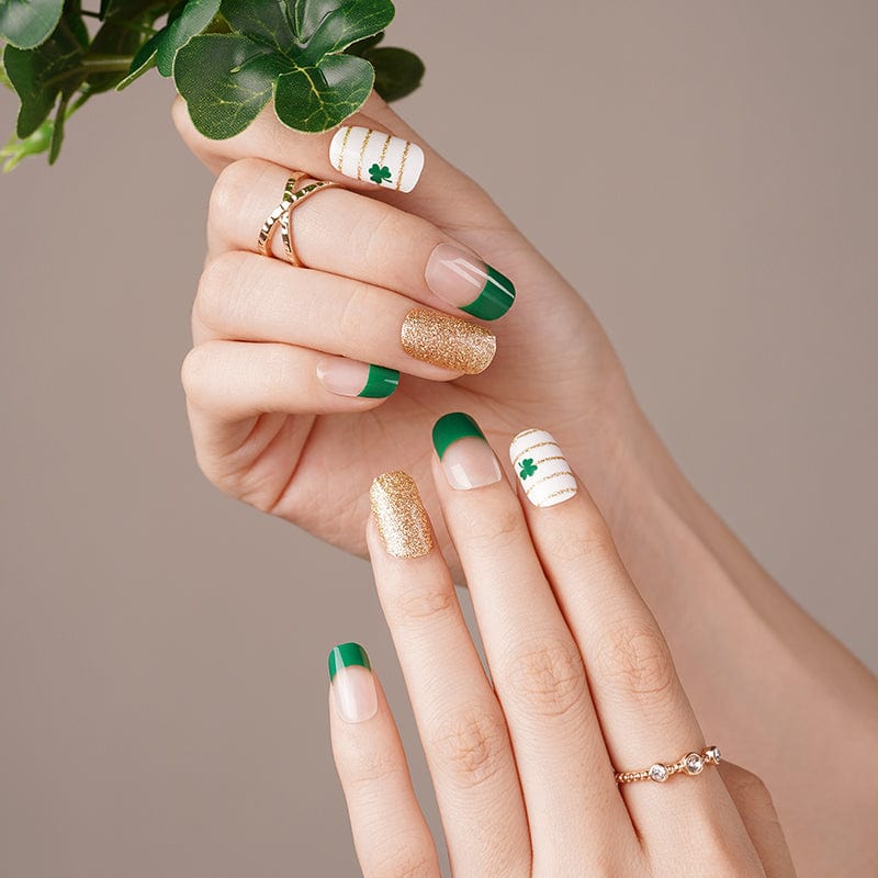 Hand wearing green and gold shamrock nail wraps with French tips for festive manicure