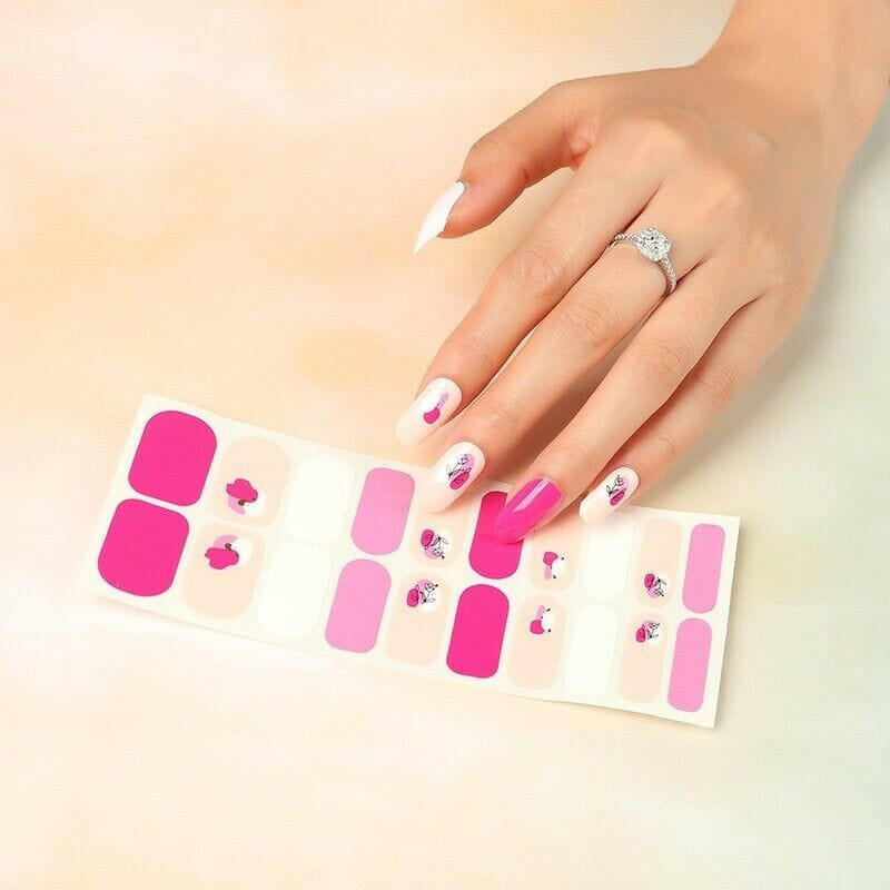 Hand reaching for magenta and pink floral nail wraps with rose patterns on sheets