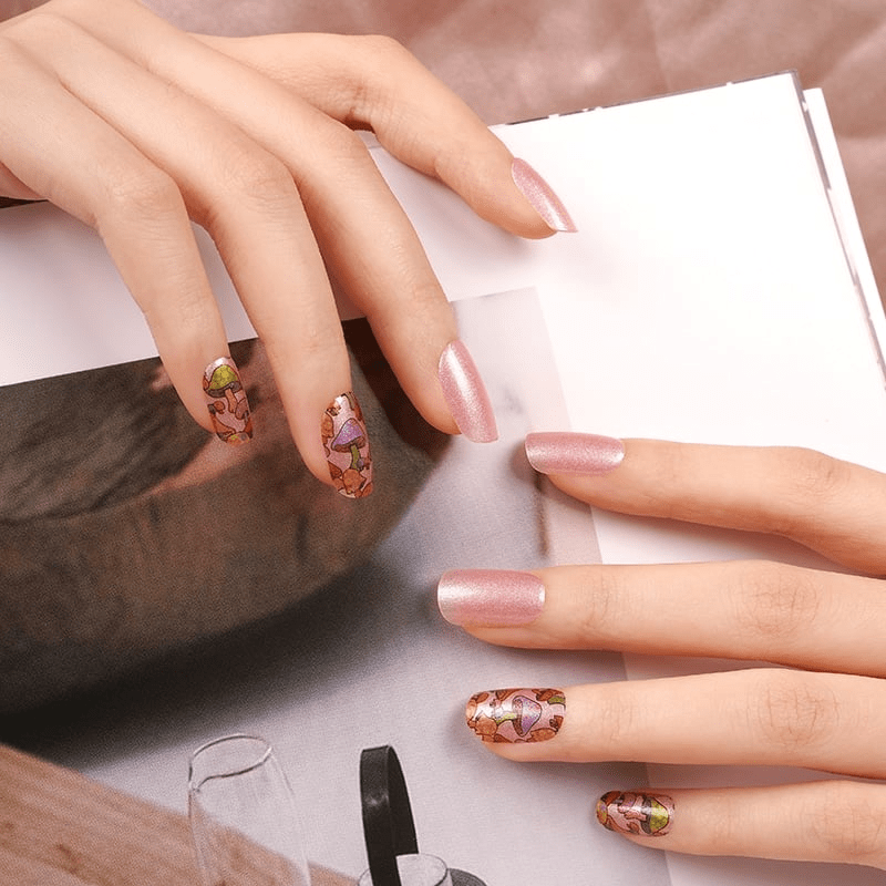 Whimsical mushroom nail wraps on hand with soft pink base and fairytale toadstool design