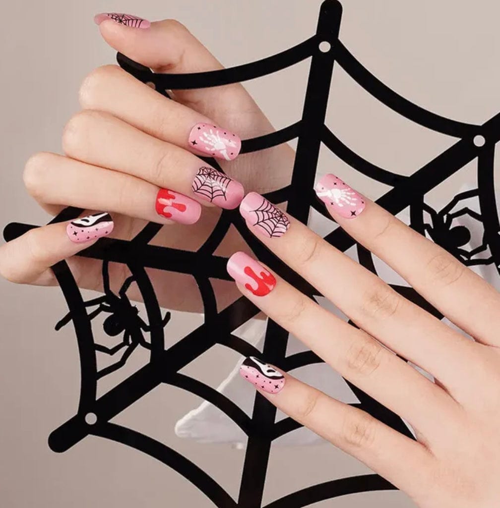 Halloween themed nail wraps on hand showing pink base with spider web and ghost designs