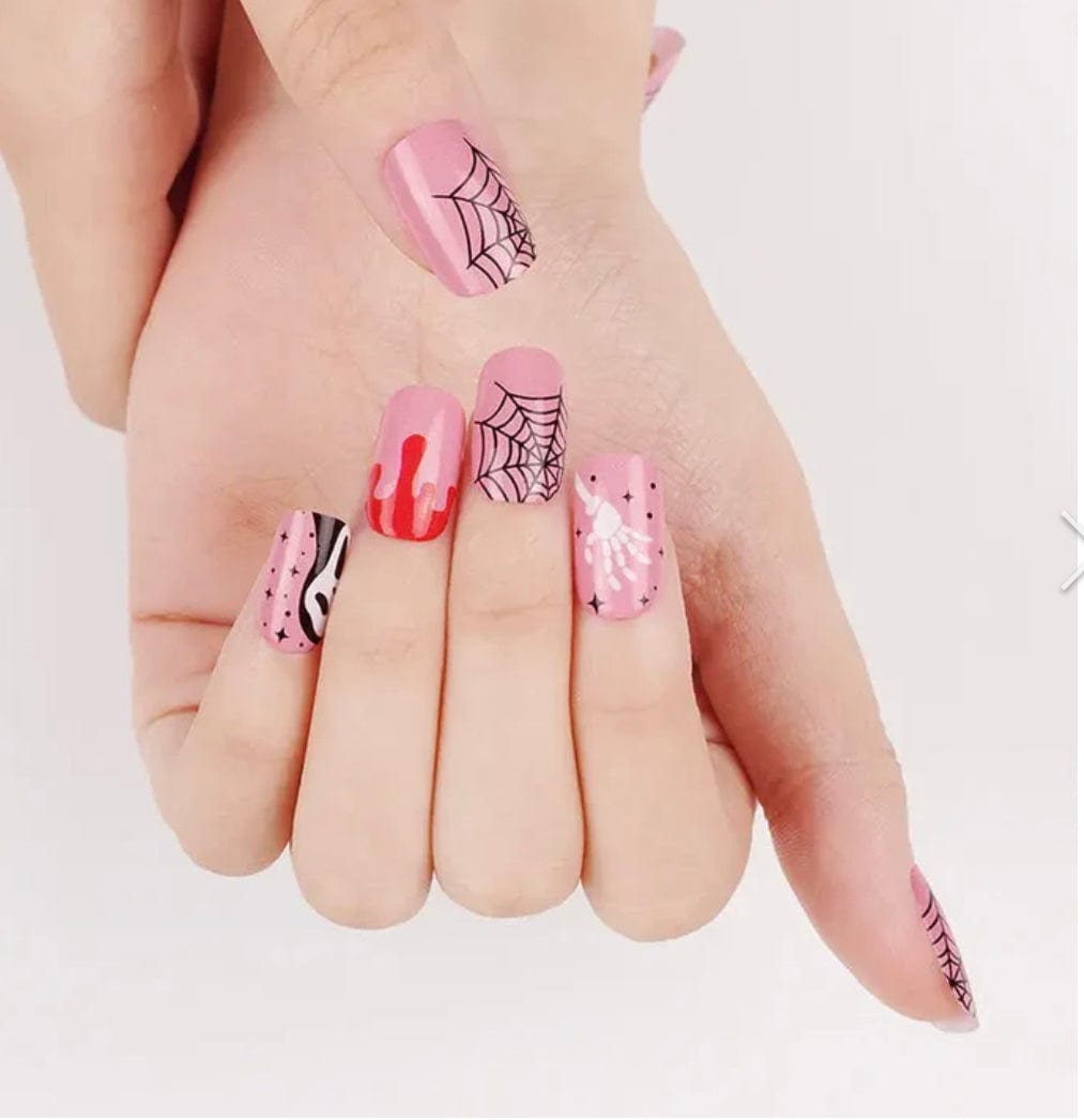 Hand displaying Halloween nail art with pink ghost faces, red drips and spider web patterns