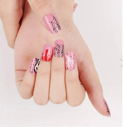 Hand displaying Halloween nail art with pink ghost faces, red drips and spider web patterns