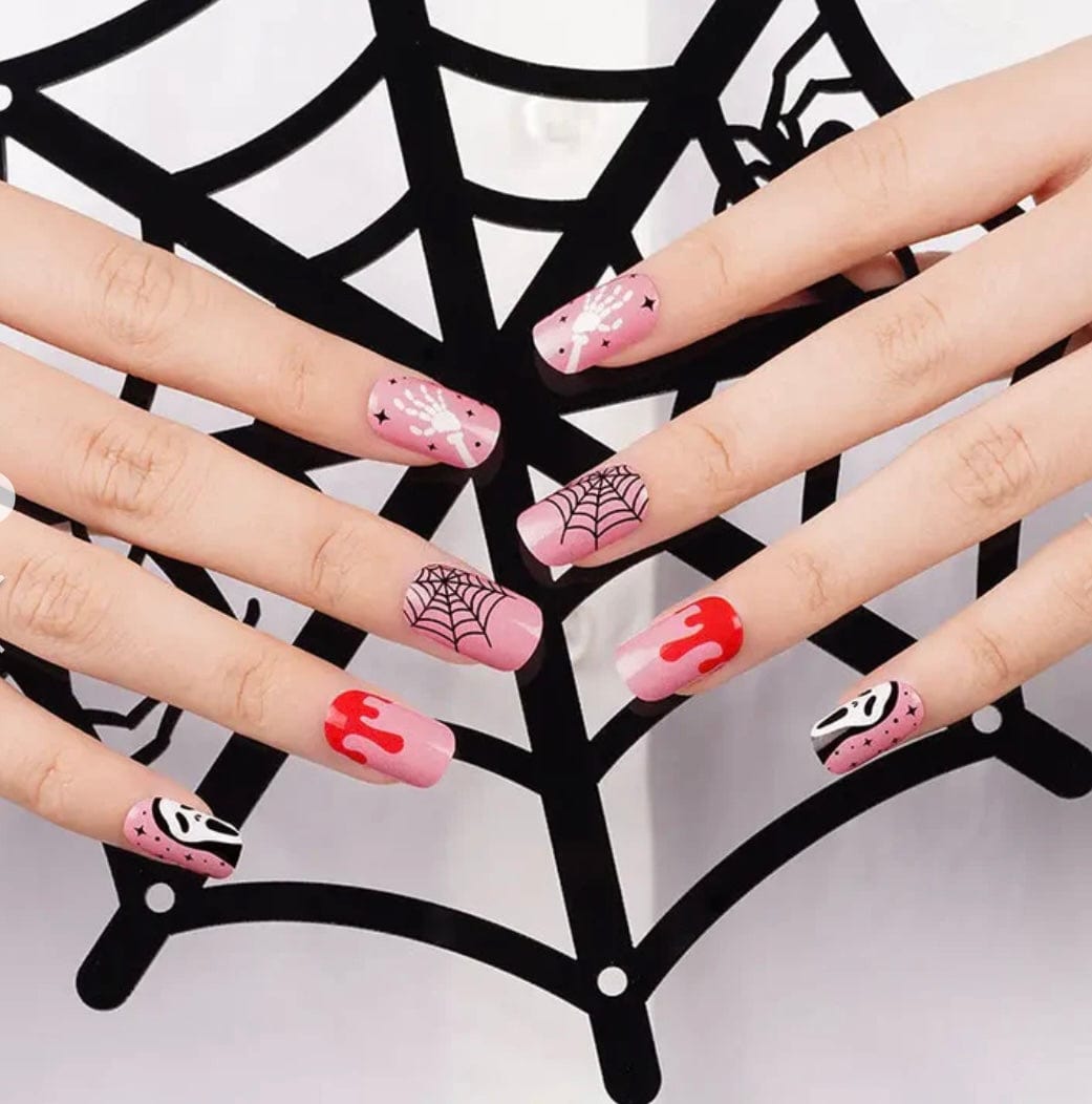 Hand wearing Halloween nail art with pink ghost faces, spider webs and red blood drips