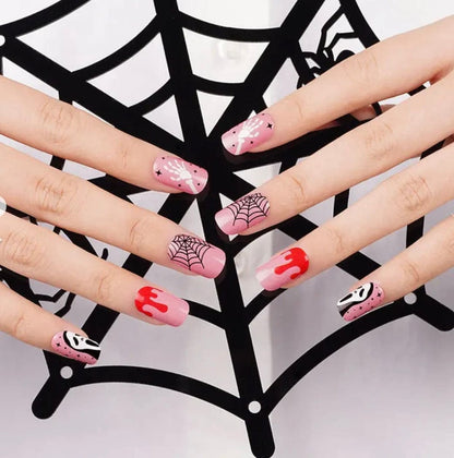 Hand wearing Halloween nail art with pink ghost faces, spider webs and red blood drips