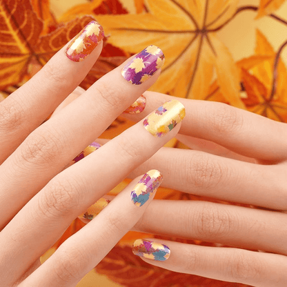 Autumn maple leaf nail wraps on hand showing orange purple yellow leaf patterns