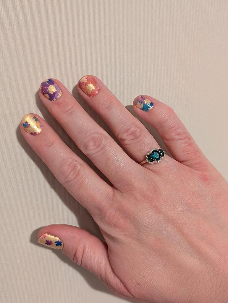 Colourful maple leaf nail art wraps displayed on hand with autumn foliage design