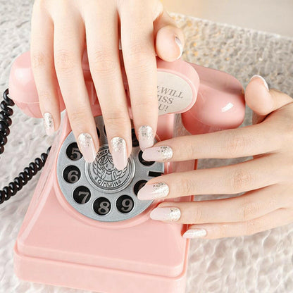 Hands with pink shimmer nail wraps holding vintage rotary phone for bridal manicure