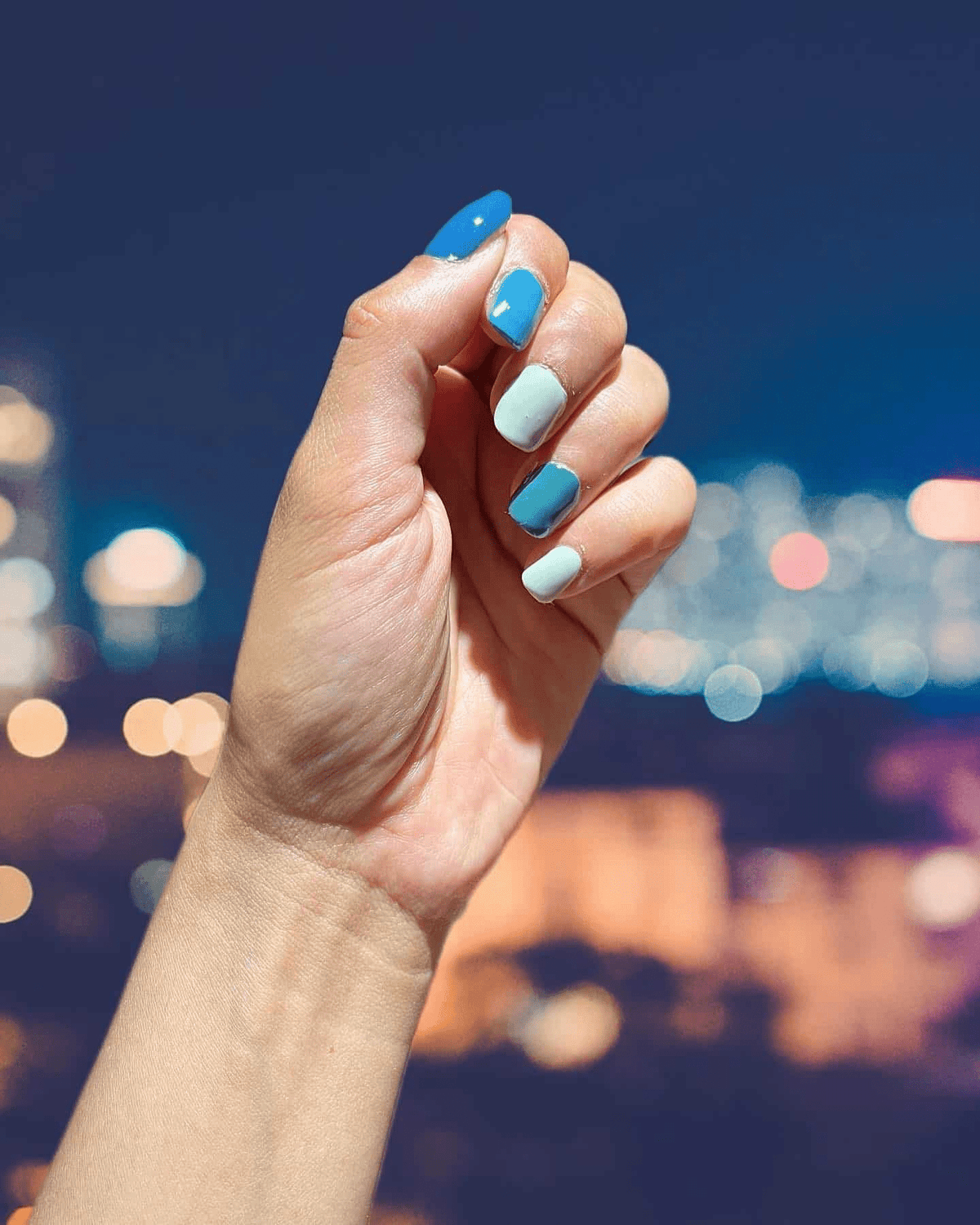 Blue and sage green ombre nail wraps on hand against city lights backdrop