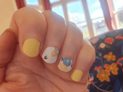Hand showing yellow and floral daisy nail wraps for at-home manicure