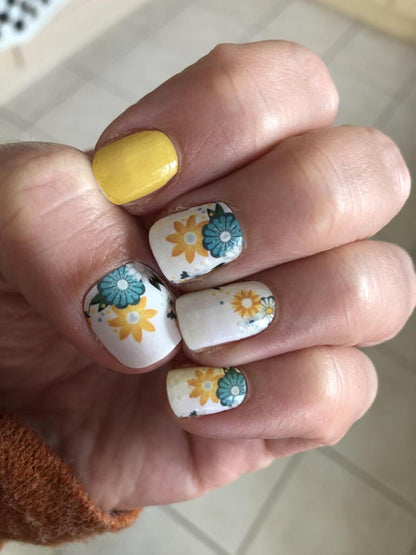 Hand displaying yellow and white floral nail wraps with blue daisy pattern