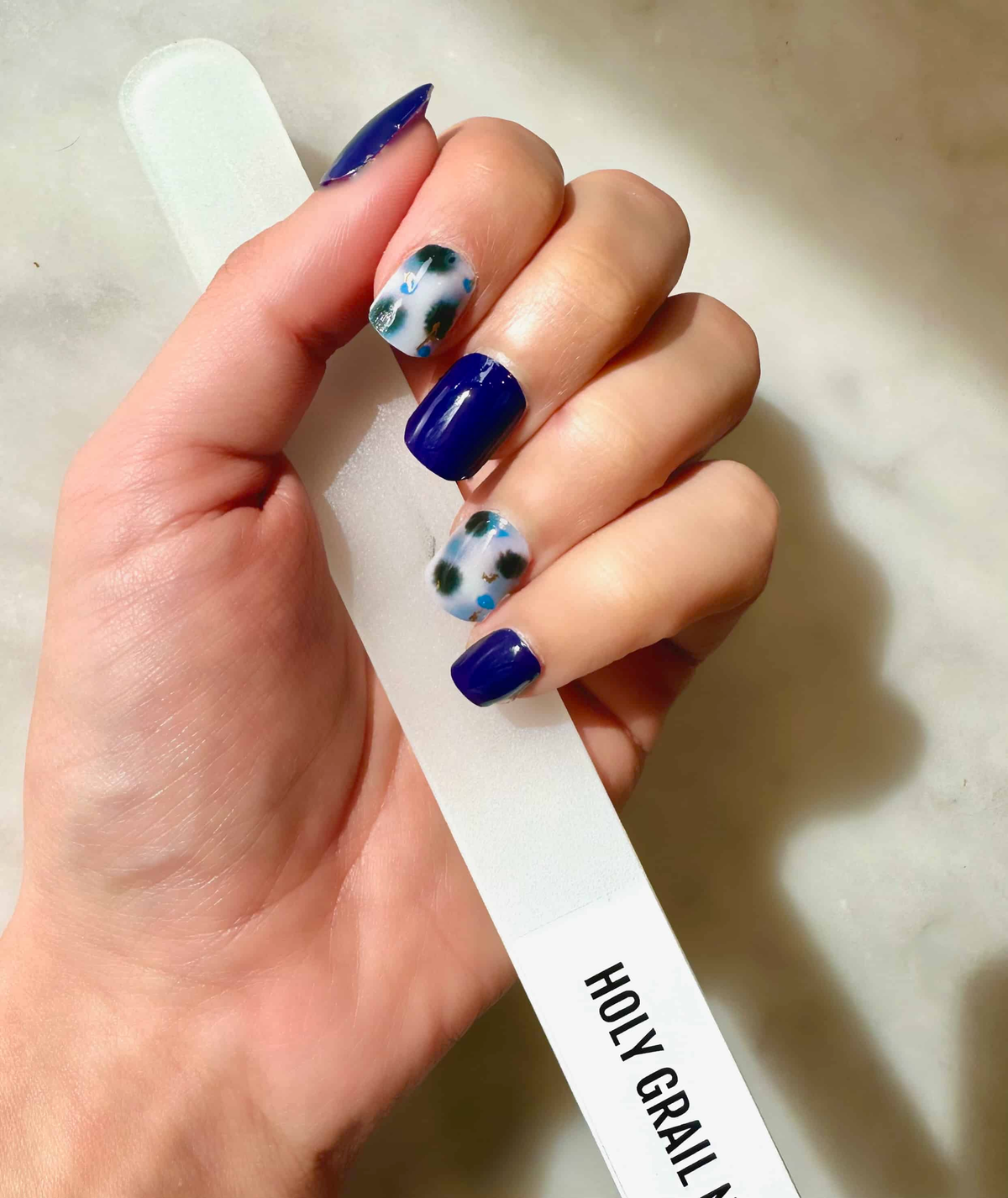 Navy blue and abstract terrazzo pattern nail wraps on hand showcasing at-home manicure design