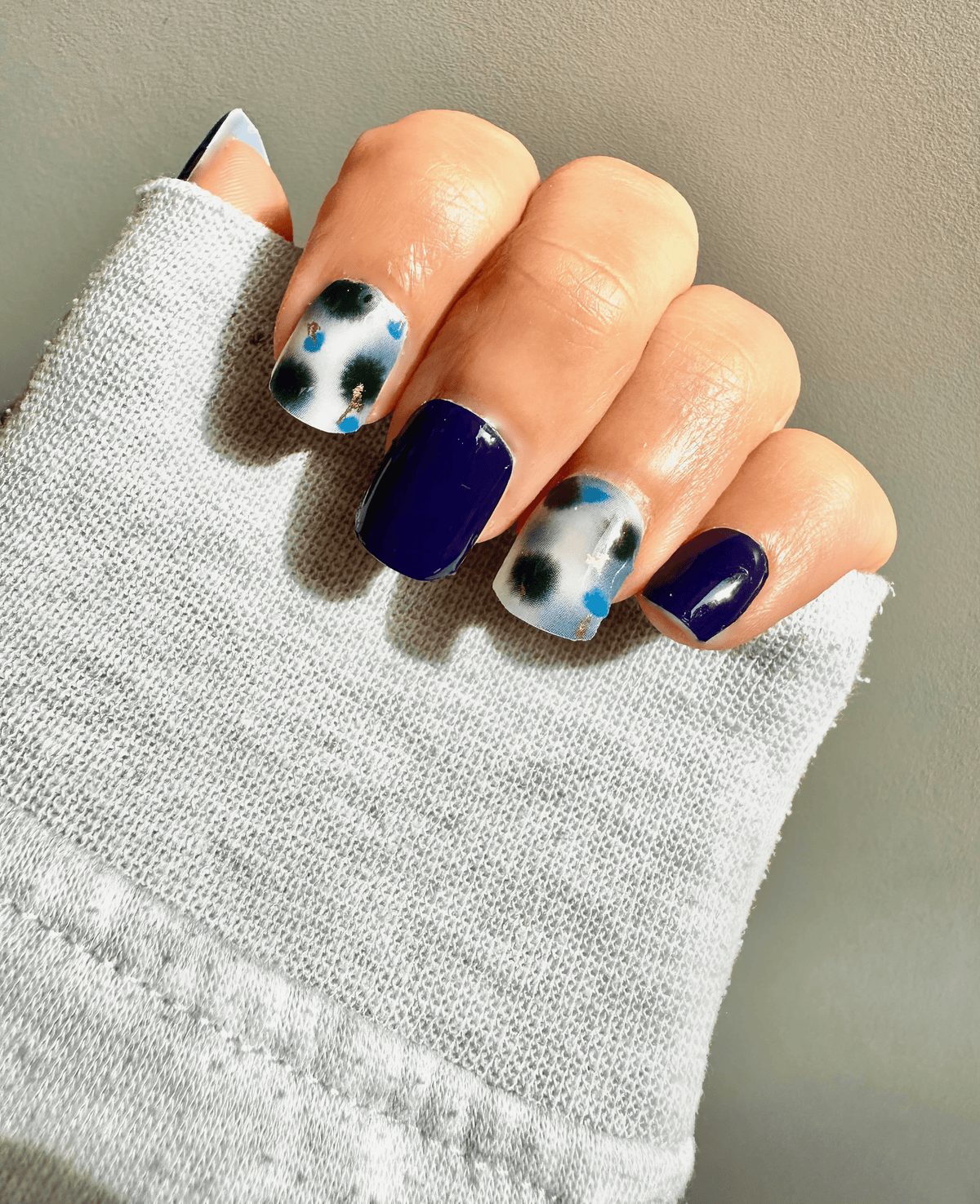 Contemporary blue and gold abstract nail wraps on hand with minimalist terrazzo pattern