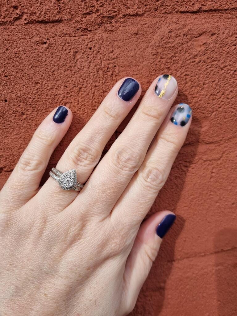 Navy and gold foil terrazzo nail wraps on hands against terracotta wall background