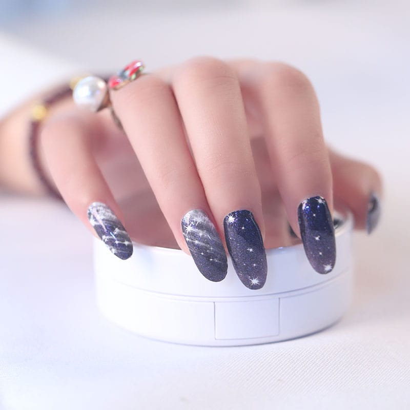 Hand wearing black cosmic nail wraps with silver stars and sparkle details