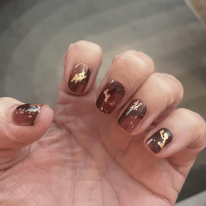 Glossy burgundy marble nail wraps with gold accents on hand autumn manicure