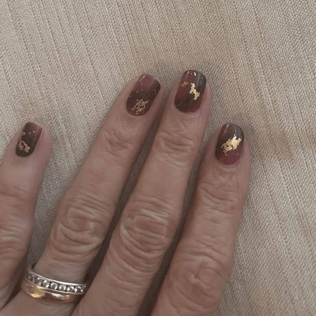 Dark burgundy marble effect nail wraps with metallic gold veining on hand