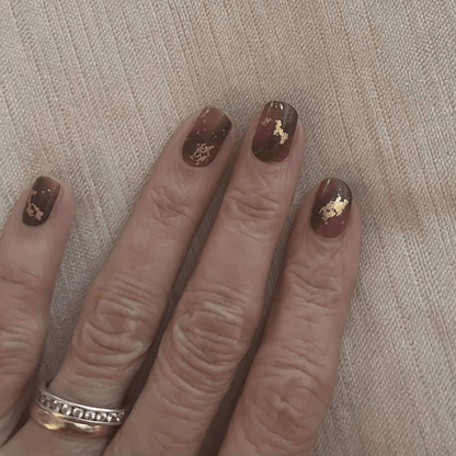 Dark burgundy marble effect nail wraps with metallic gold veining on hand