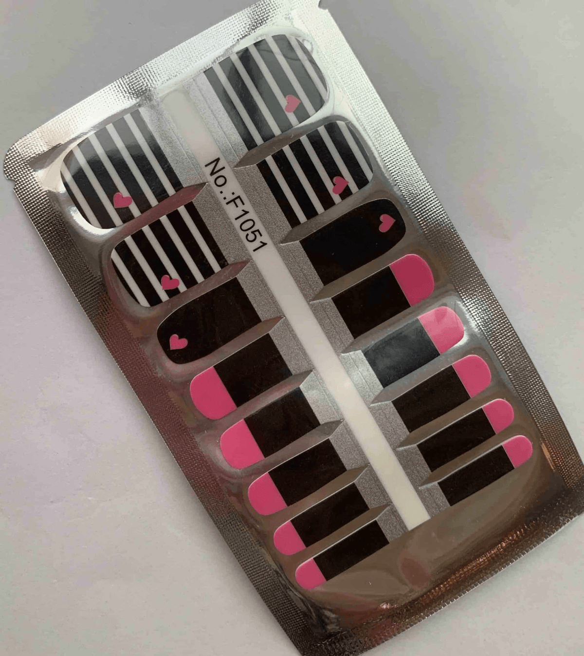 Black and white striped nail wraps with pink hearts in packaging for pedicures