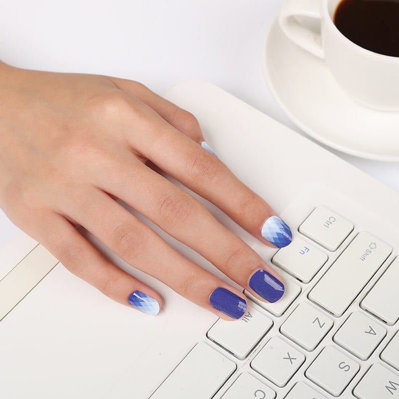 Hand with navy blue nail wraps, some with ombre diamond pattern, resting on laptop keyboard
