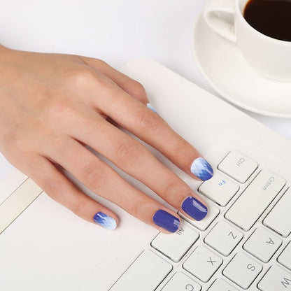 Hand with navy blue nail wraps, some with ombre diamond pattern, resting on laptop keyboard