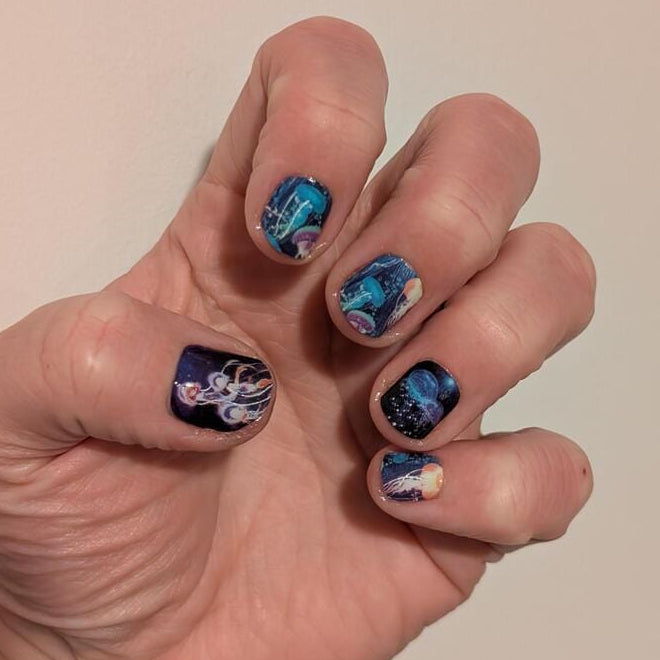 Hand displaying blue jellyfish nail wraps with iridescent underwater sea life nail art