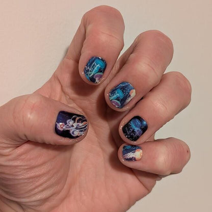 Hand displaying blue jellyfish nail wraps with iridescent underwater sea life nail art