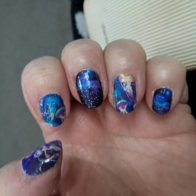 Blue iridescent jellyfish nail wraps on hand showcasing holographic underwater nail art design