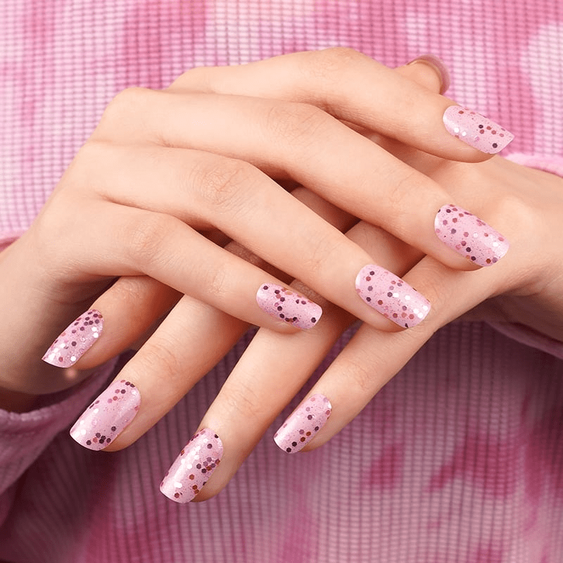 Pink speckled nail wraps with dot pattern on hands against gingham background for at-home manicure