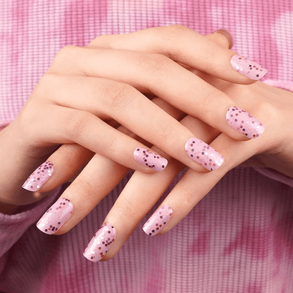 Pink speckled nail wraps with dot pattern on hands against gingham background for at-home manicure