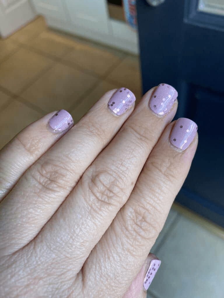 Close-up of pink nail wraps with black speckled pattern applied to fingernails showing glossy finish