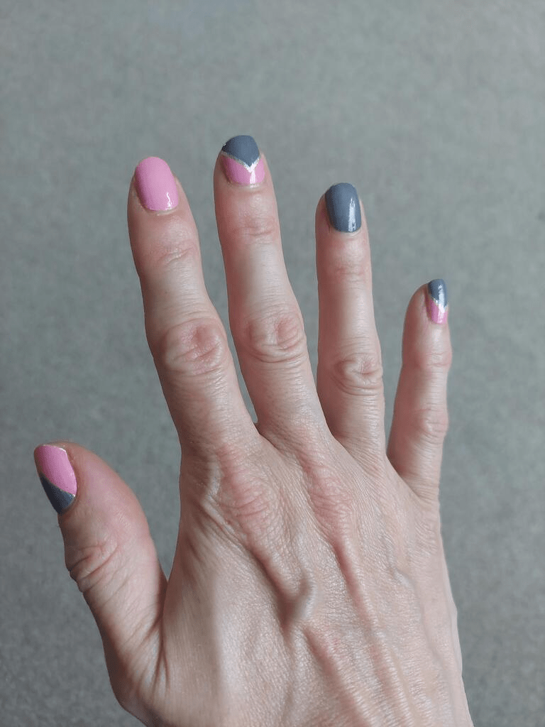 Hand on grey surface showing pink and grey geometric nail wraps professional manicure design