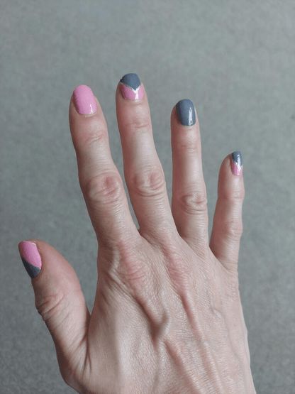 Hand on grey surface showing pink and grey geometric nail wraps professional manicure design