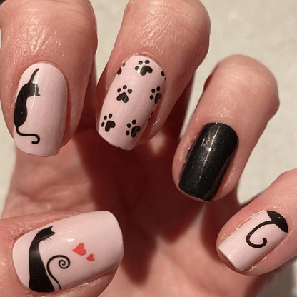 Pale pink nail wraps with black cat silhouettes, paw prints, hearts and a solid black accent nail