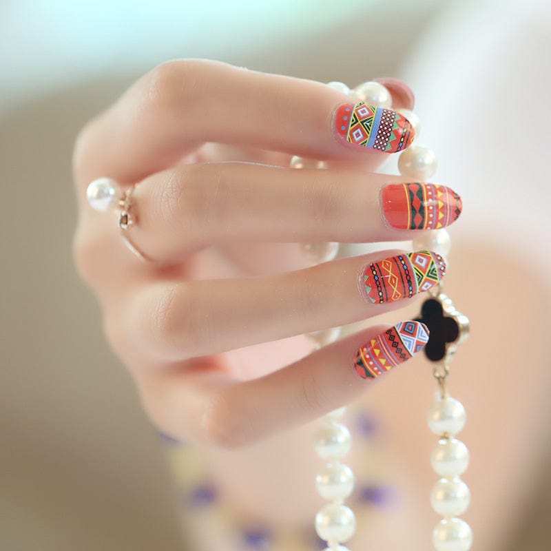 Hand wearing vibrant orange and red geometric pattern nail wraps with tribal southwestern design