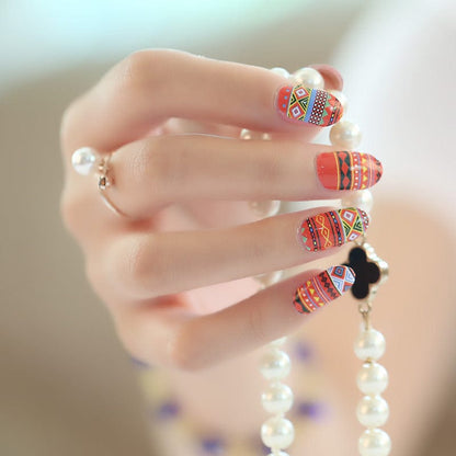 Hand wearing vibrant orange and red geometric pattern nail wraps with tribal southwestern design