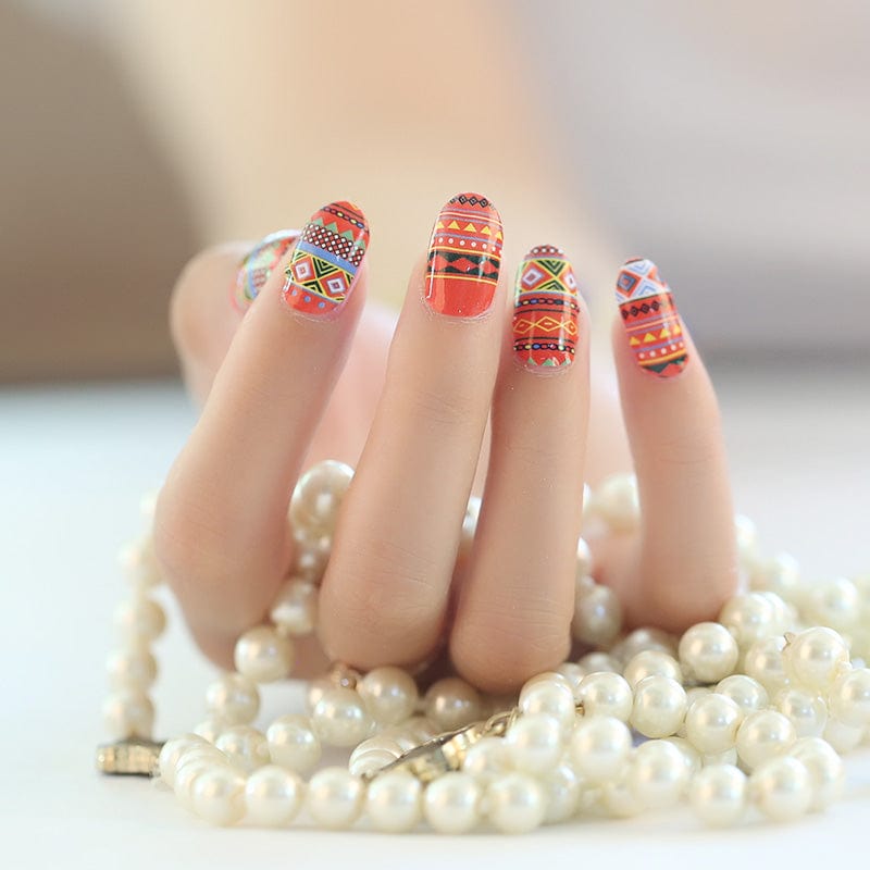 Hand with colourful geometric nail wraps in orange red tribal patterns holding pearl necklace