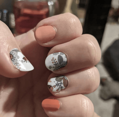 Close-up of peach and white floral bee nail wraps on hand with vintage botanical pattern