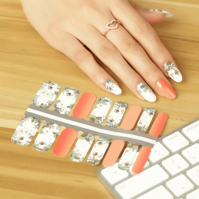 Floral bee nail wraps on hand with peach and white botanical design for at-home manicure