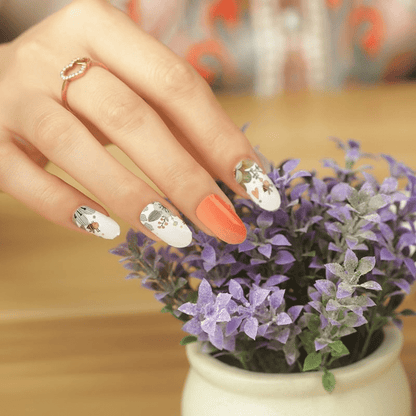 Hand wearing botanical nail art wraps with bee and floral patterns near purple flowers